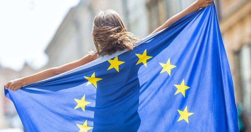 EU Flag. Cute Happy Girl With The Flag Of The European Union. Young Teenage Girl Waving With The European Union Flag In The City